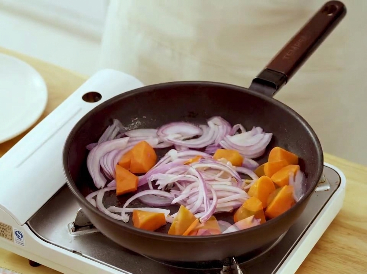 Carrot chunks and onion strips simmering in a frying pan.