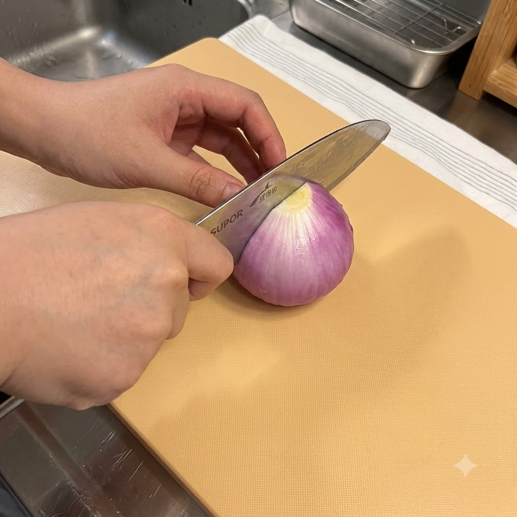A kitchen knife cutting through a red onion on a wooden cutting board.