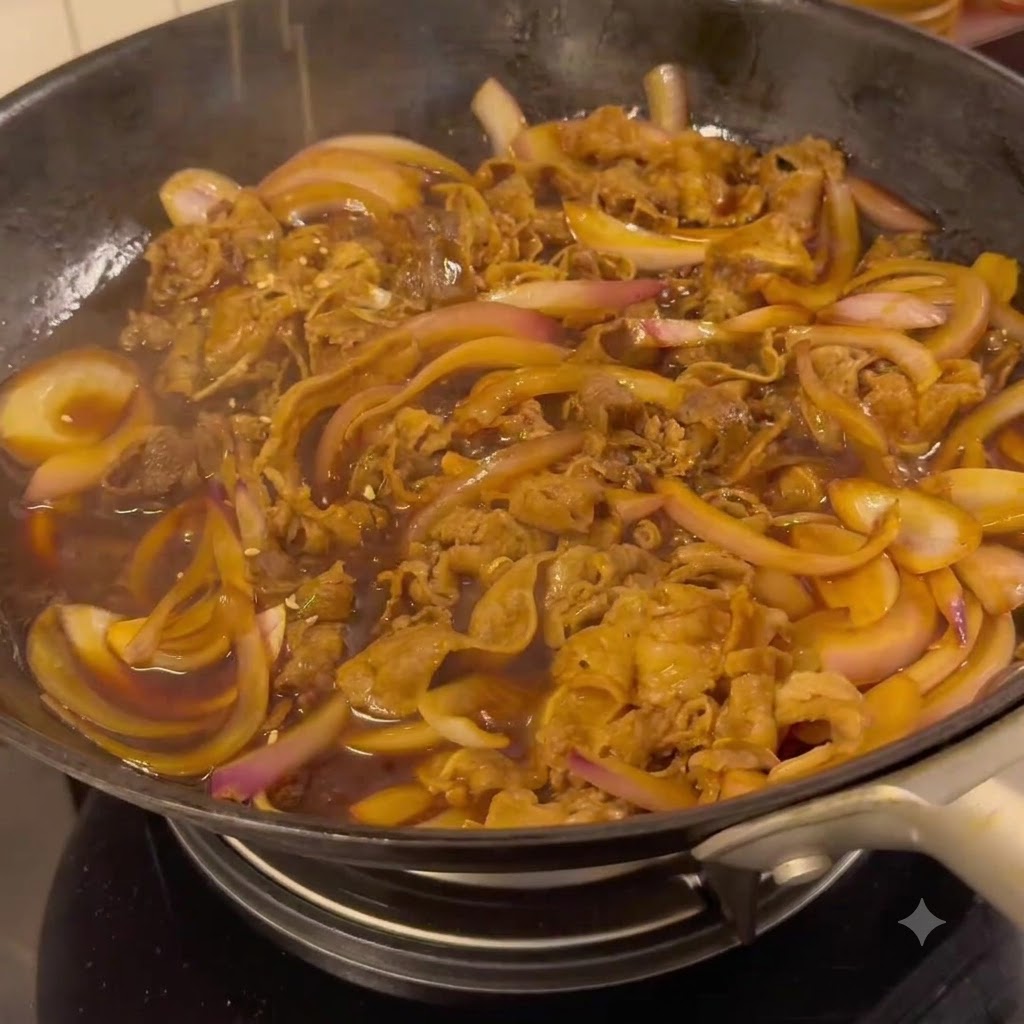Beef and onions simmering in a dark savory teriyaki sauce inside a frying pan.