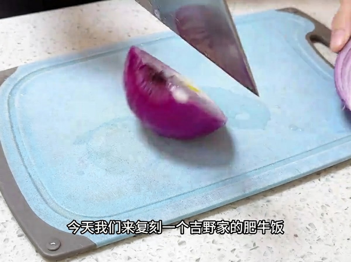 A kitchen knife slicing a red onion into thin pieces on a blue cutting board.