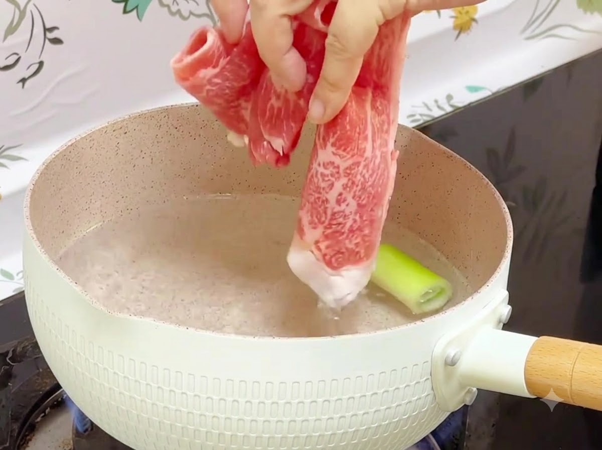 Frozen beef rolls being dropped into a pot of boiling water with a scallion piece inside.