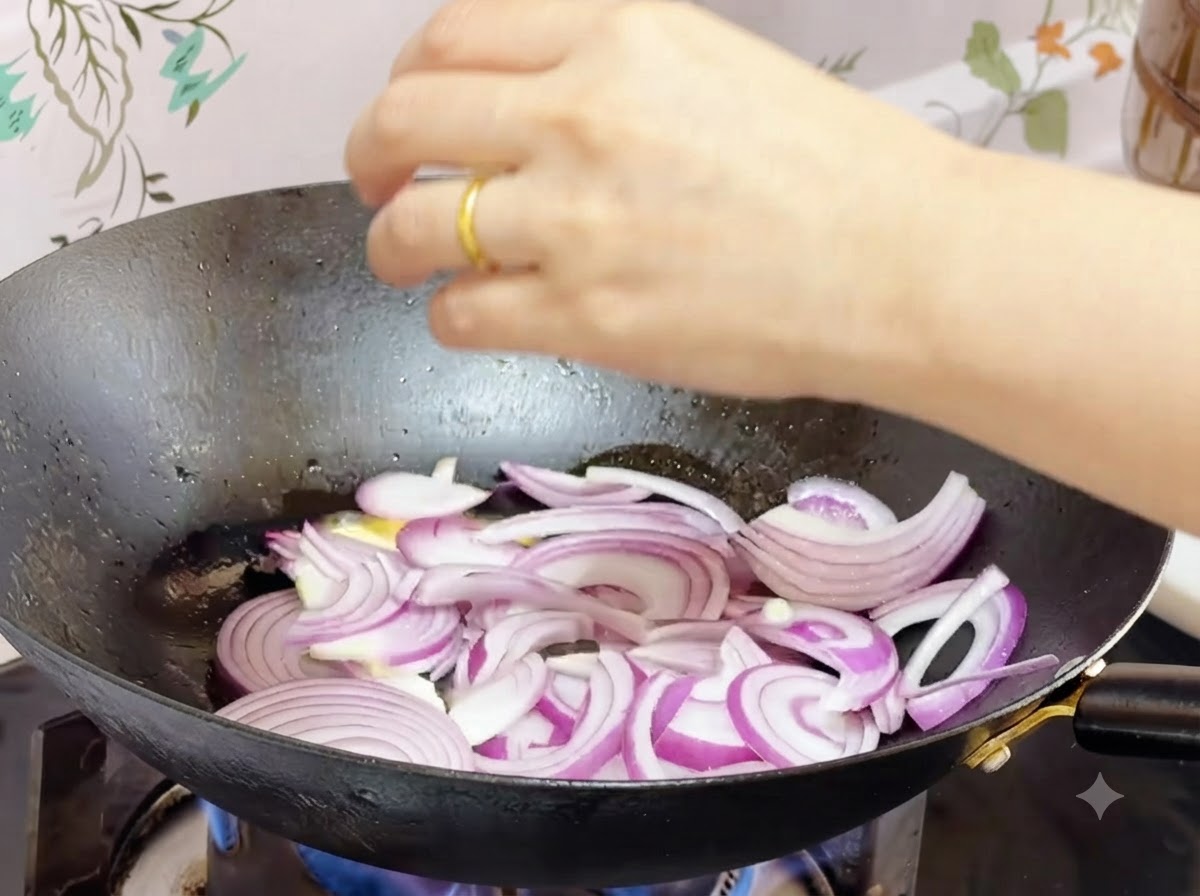 Sliced red onions stir-frying in melted butter inside a wok.