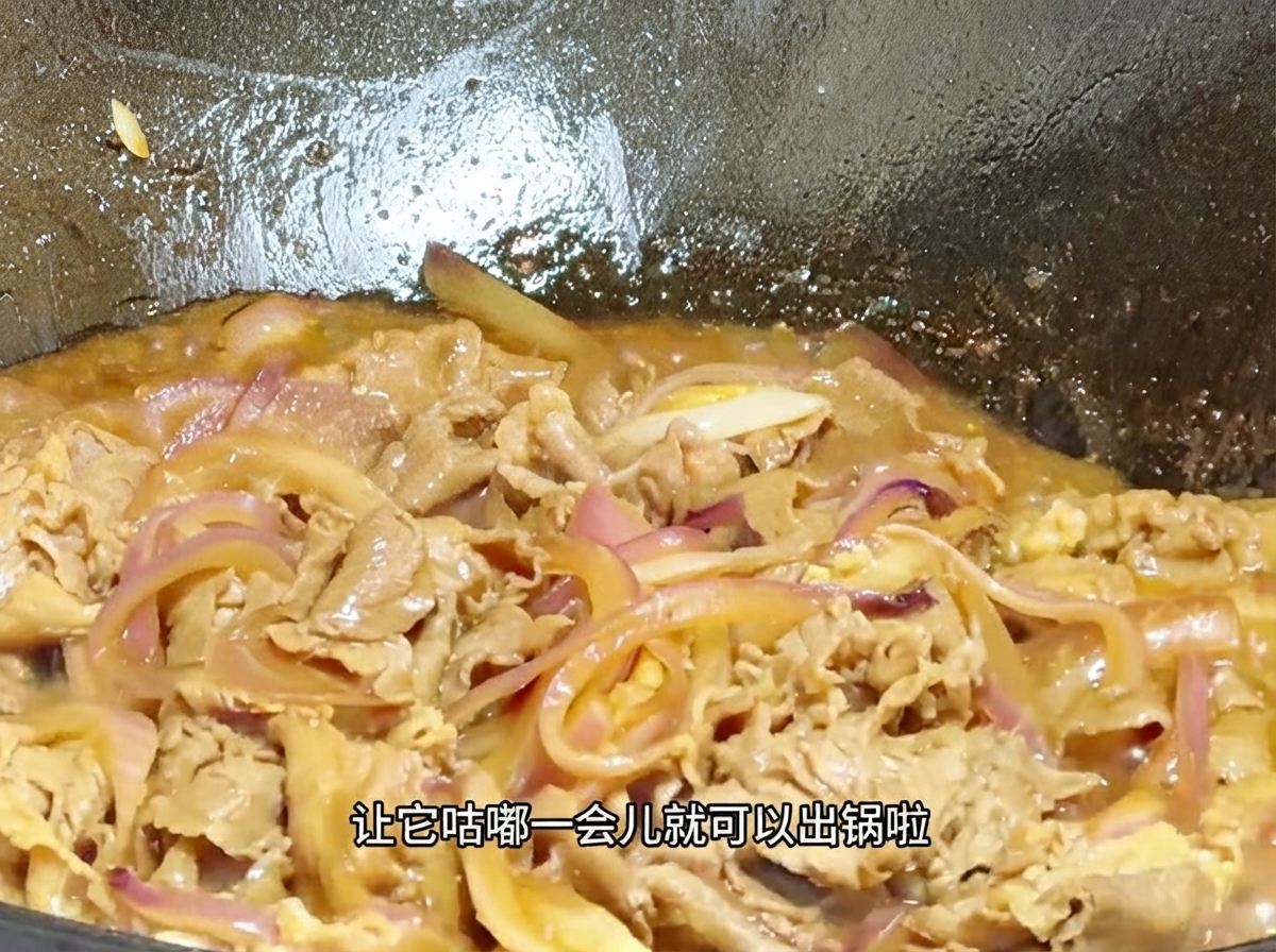 A close-up view of beef and onions simmering in a thickened bubbly sauce inside a wok.