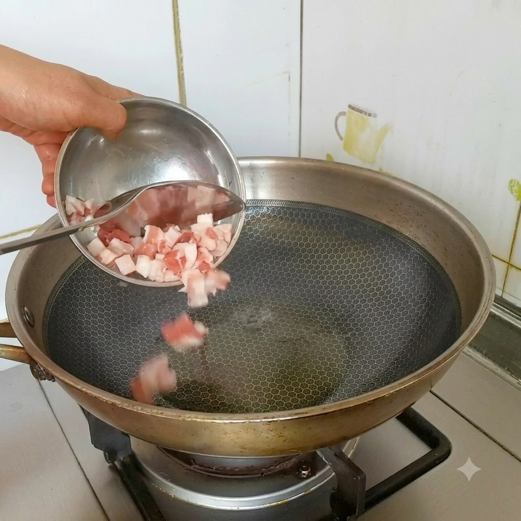 Diced pork belly being poured from a small bowl into a hot, oiled stainless steel wok.