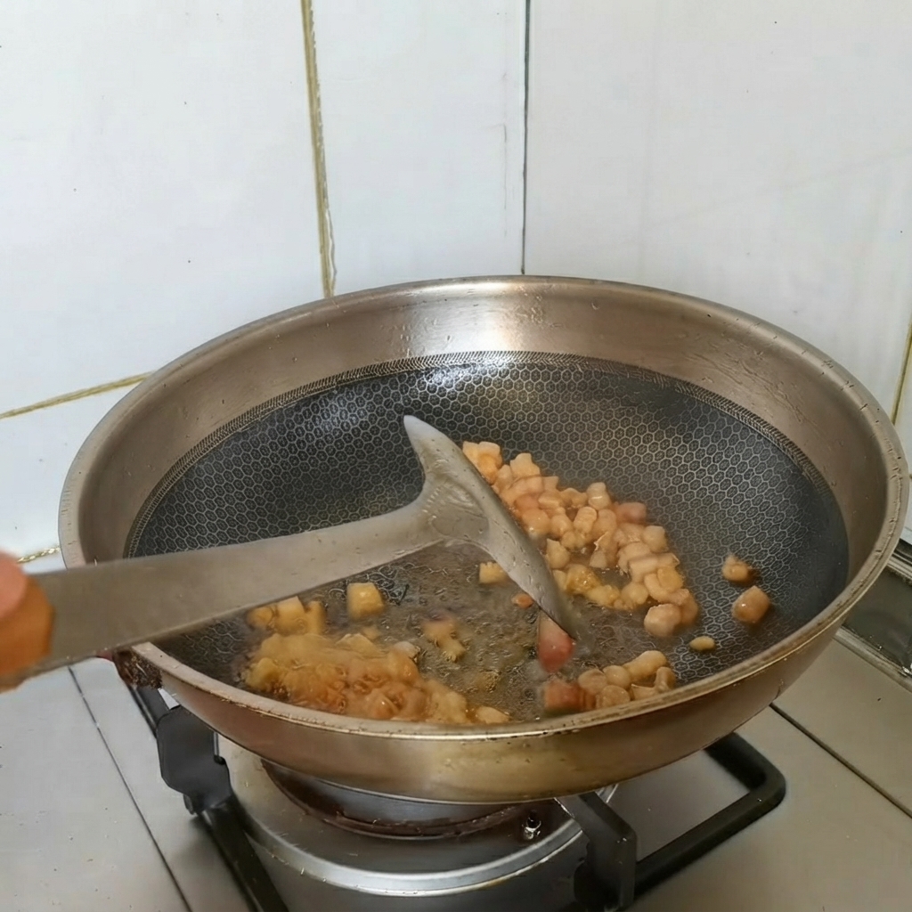 Browning pieces of pork belly being stir-fried in a wok with aromatics.
