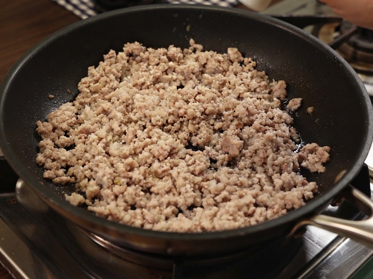 Ground black pepper and sea salt being sprinkled onto cooked minced pork in a pan.
