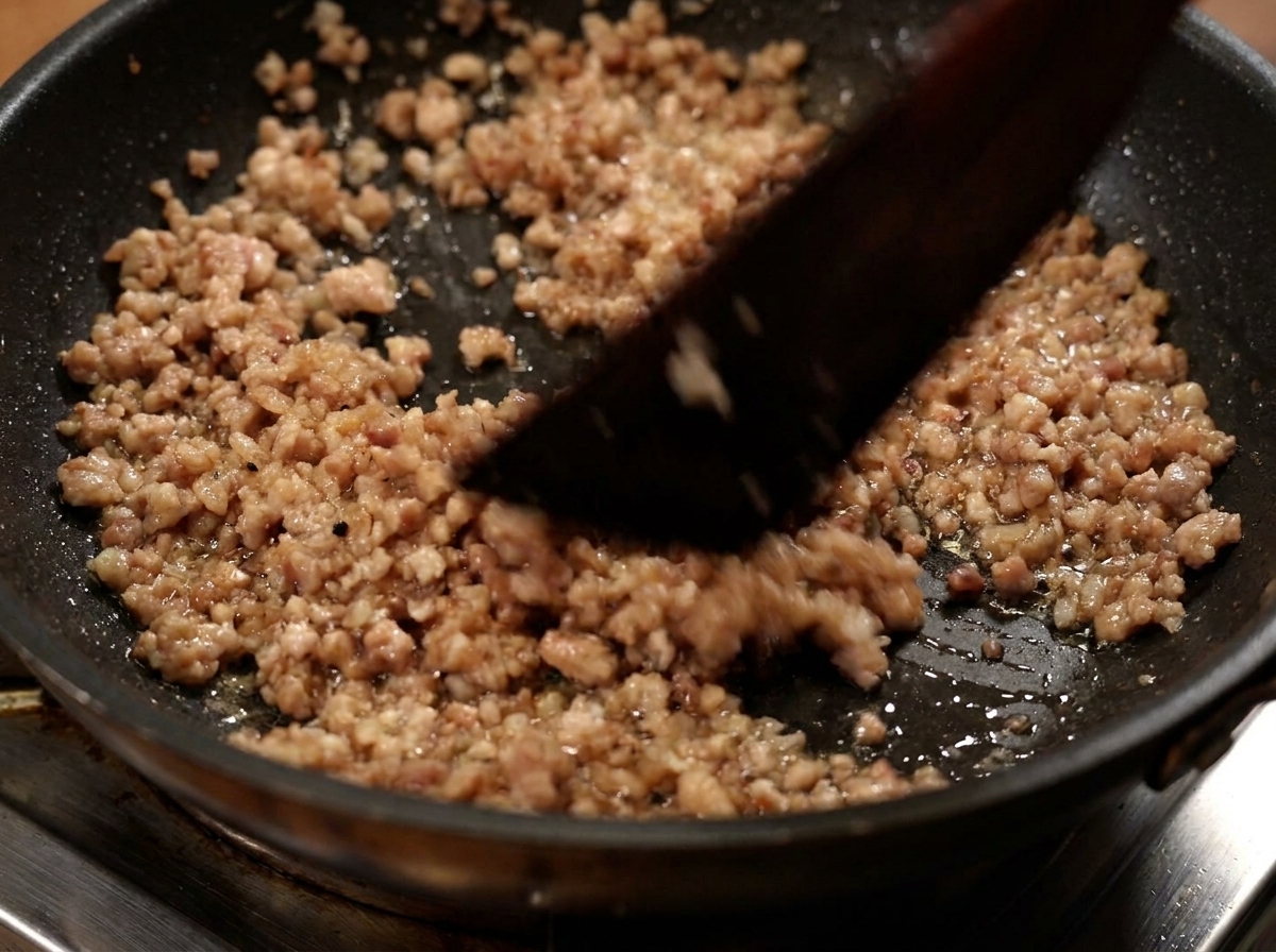 Cooked minced pork being scooped out of a frying pan with a spatula.