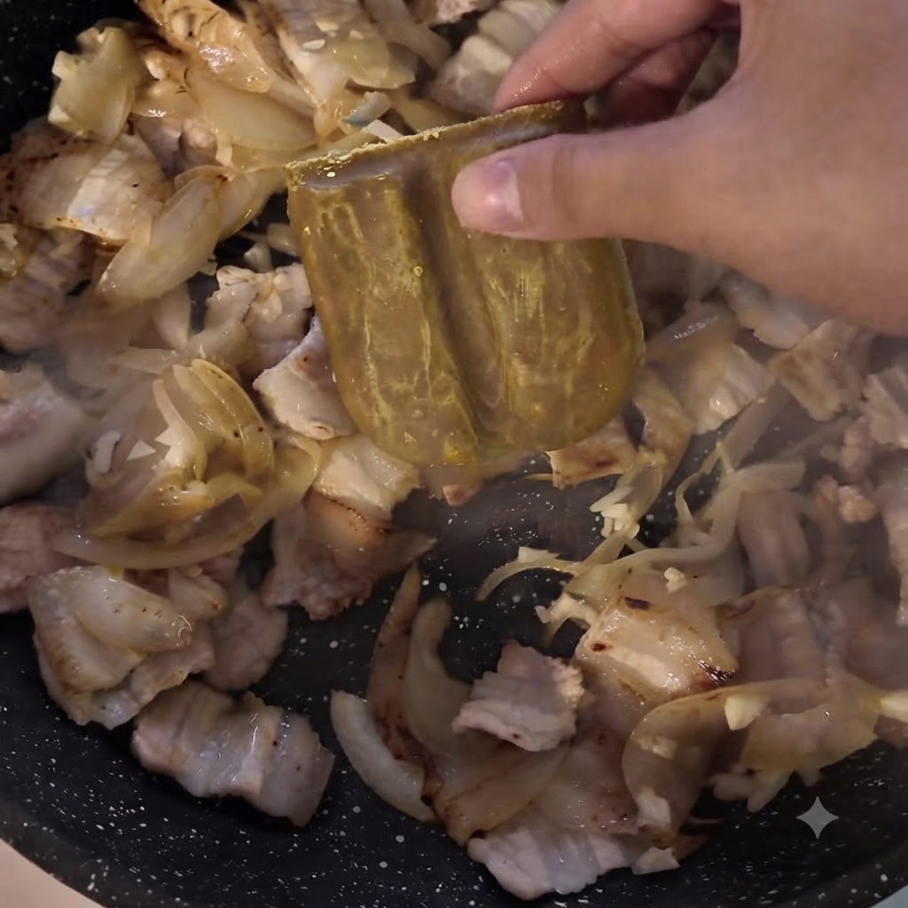 A block of curry paste being added to the pan containing meat and onions.