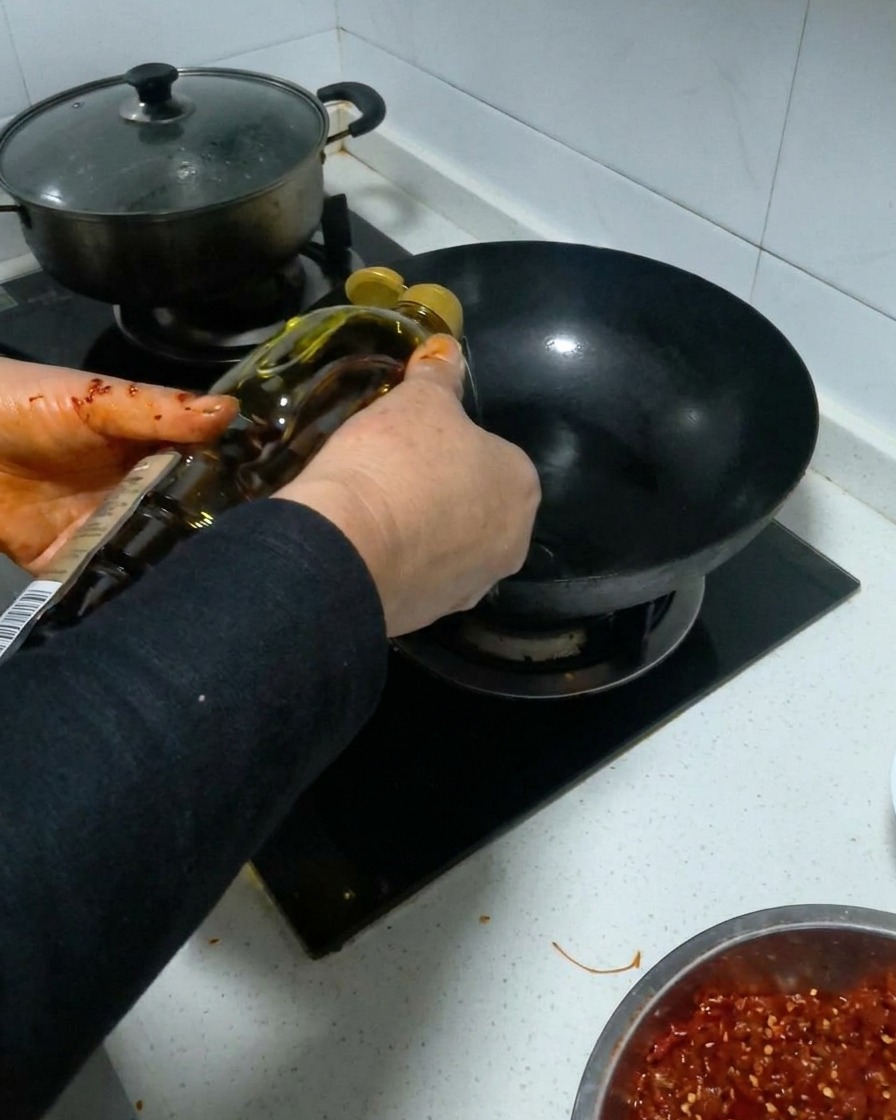 Cooking oil being poured from a bottle into a black heated wok.