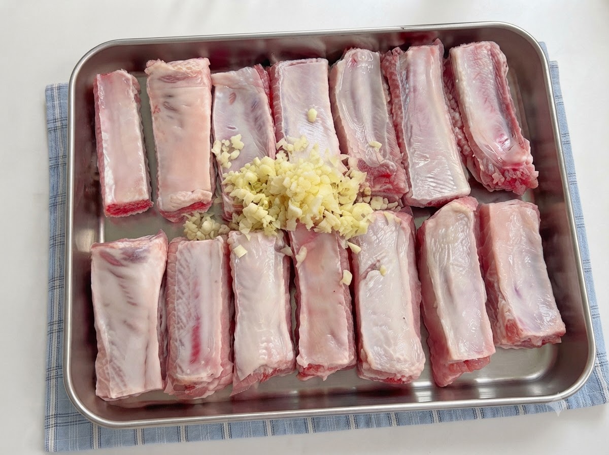 Sauces being poured from a spoon over seasoned spare ribs with minced garlic.