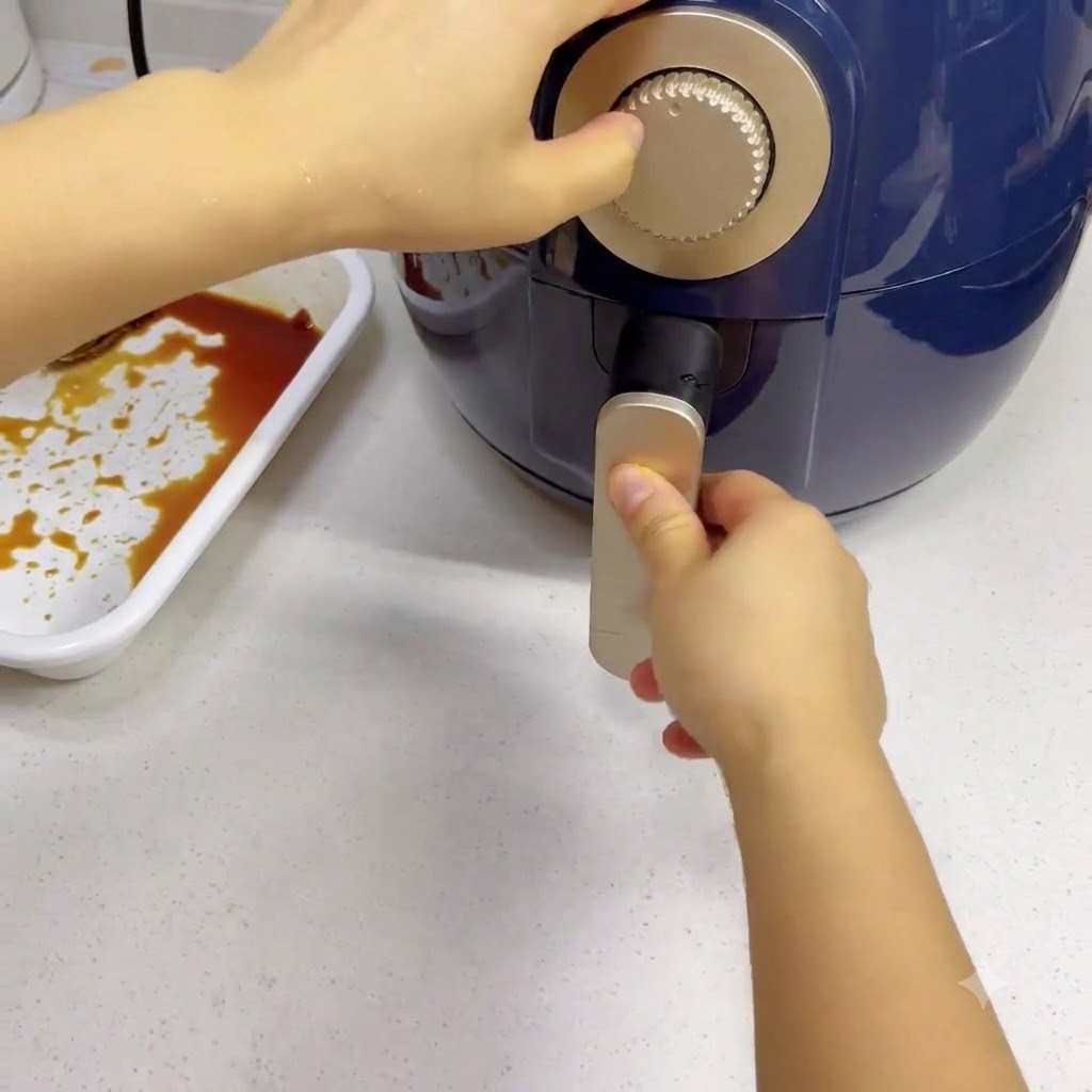 A hand turning the silver timer dial on a dark blue air fryer.