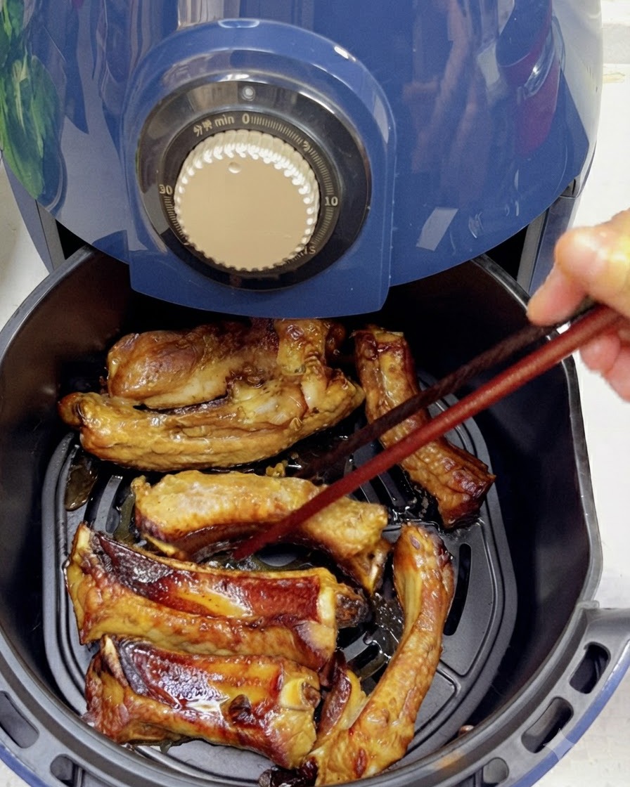 Using chopsticks to flip partially cooked, browned pork ribs inside an air fryer basket.