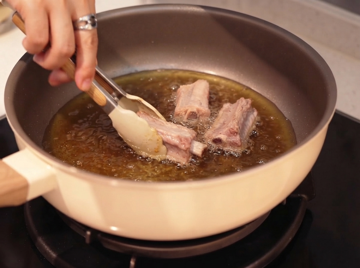 Pork ribs being pan-fried in hot oil using tongs.