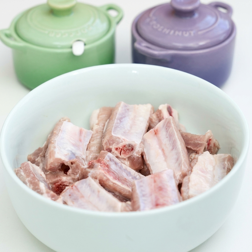 Raw pork ribs in a white bowl being seasoned with garlic, soy sauces, oyster sauce, and spices.