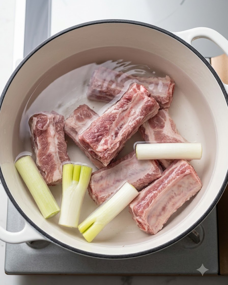 Fresh pork ribs resting in a pot of cold water with green onions and aromatics before boiling.
