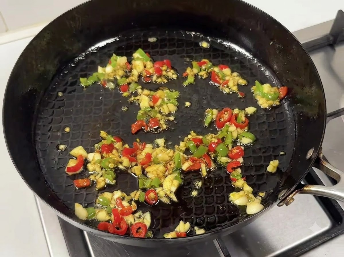 A pan containing sautéed garlic and chili mixture mixed with a savory sauce blend.