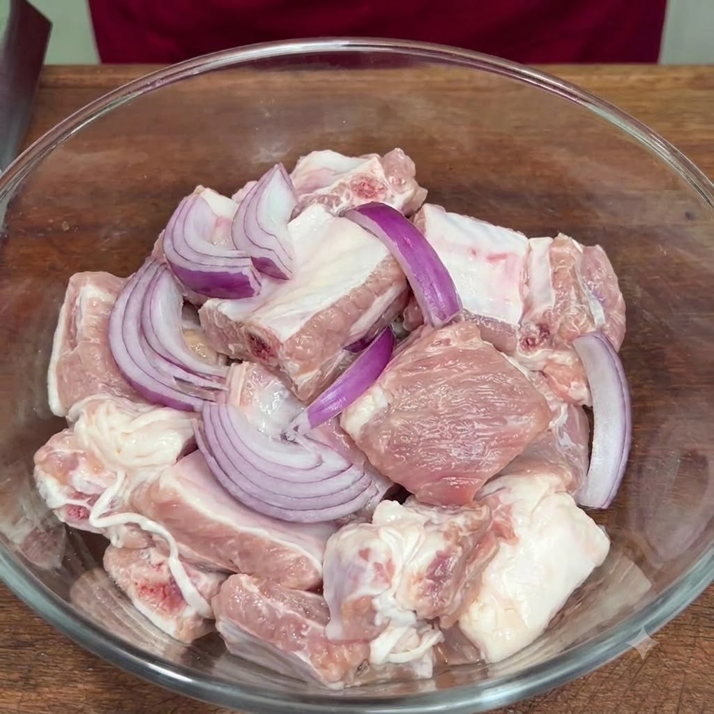 Sliced red onion and seasonings added to the raw ribs inside a glass bowl.