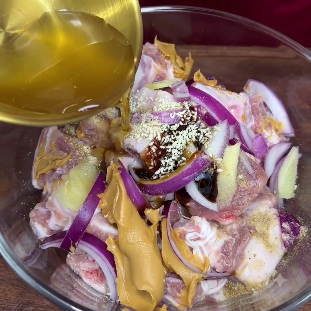 Golden garlic juice being poured from a ladle into the glass bowl containing the seasoned pork ribs and other marinade ingredients.
