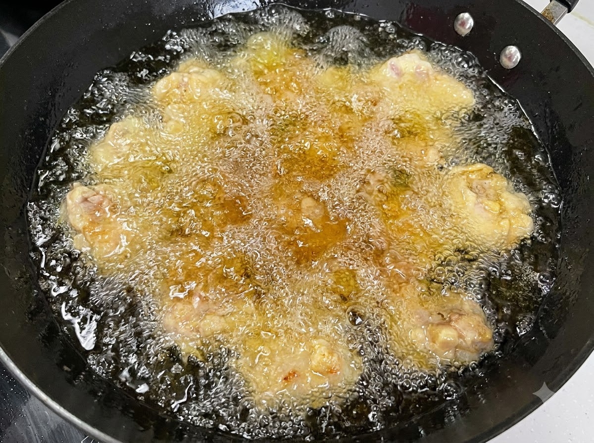 Multiple pork rib pieces deep-frying in hot, bubbling oil inside a black wok.