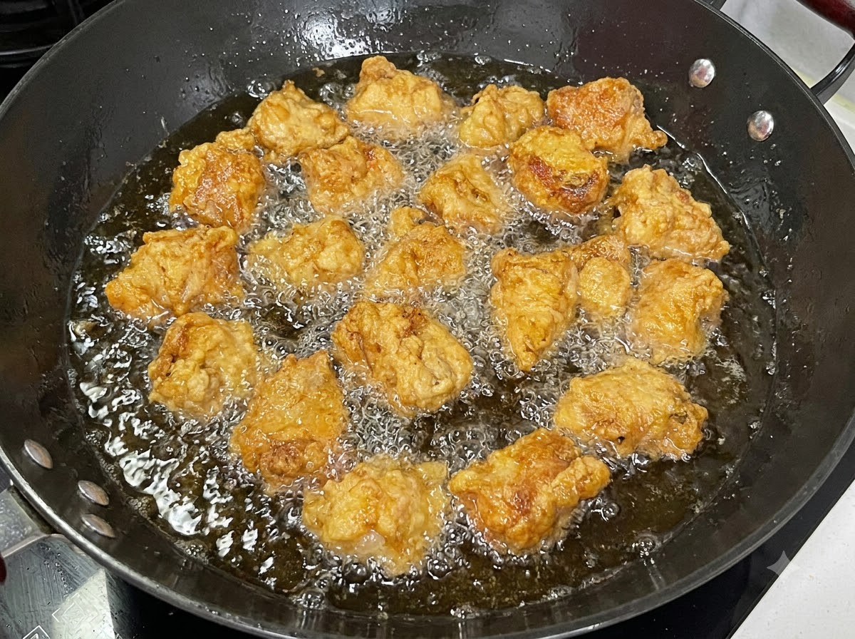 Pieces of coated pork ribs deep-frying in a black wok filled with bubbling oil.