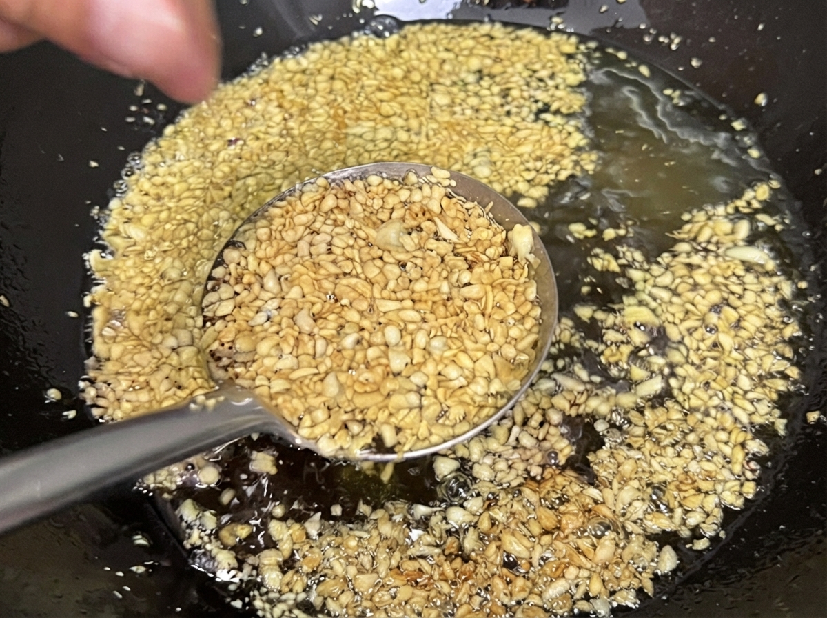 Minced garlic frying in oil inside a wok, turning a crispy, light golden yellow.