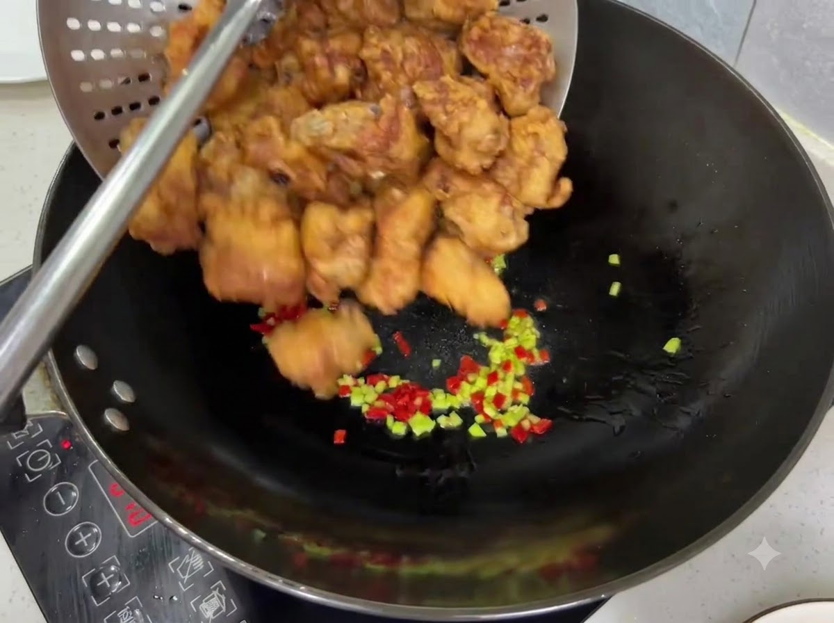 Crispy golden fried pork ribs being poured from a strainer into a wok with chilies.