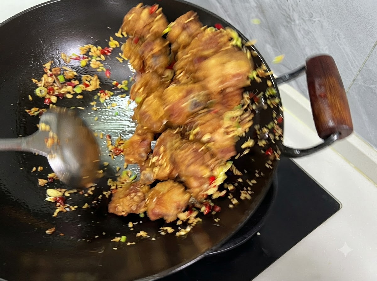 Ribs, chilies, and garlic being tossed together with a ladle inside a wok.