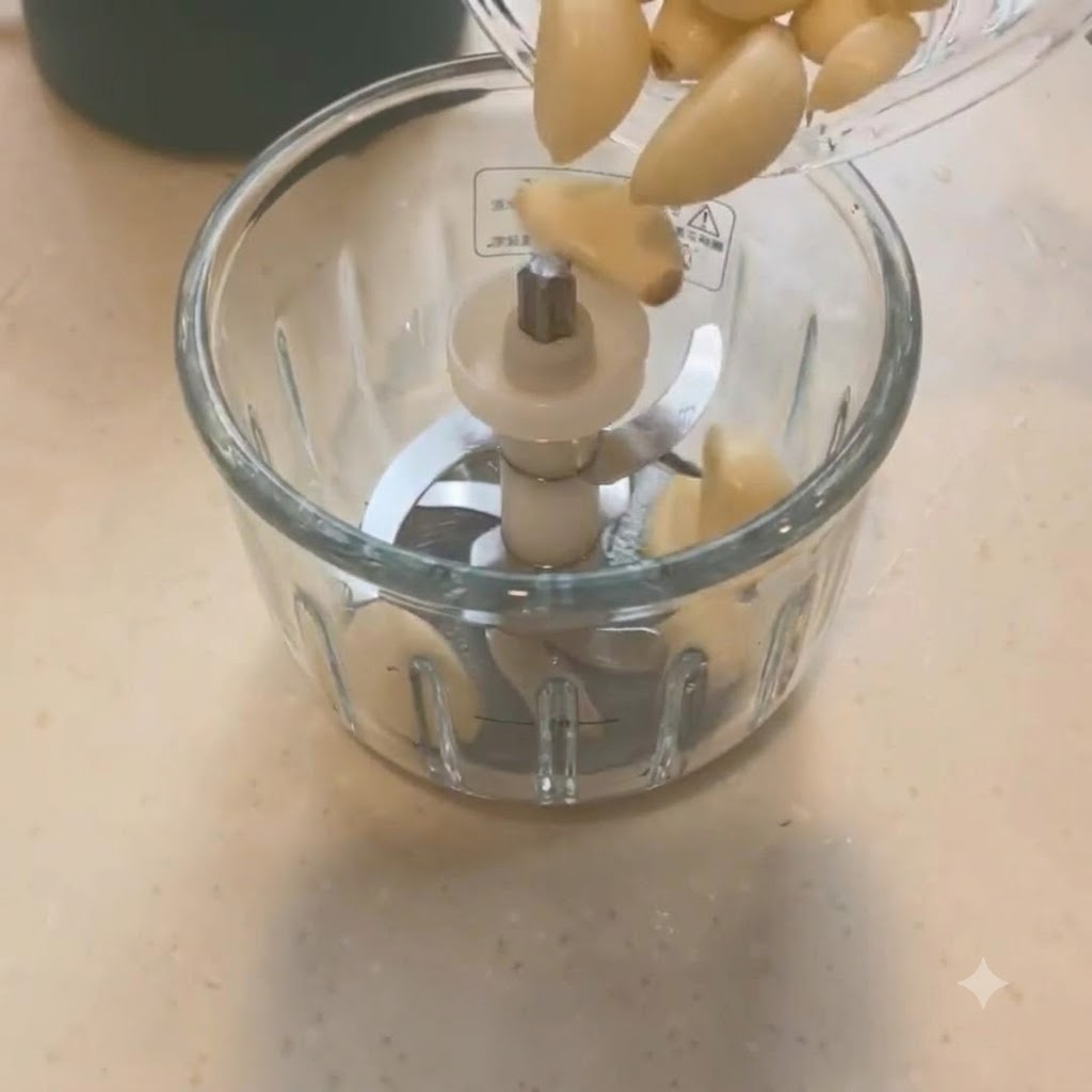 Garlic cloves being poured into a mini food chopper with blades.