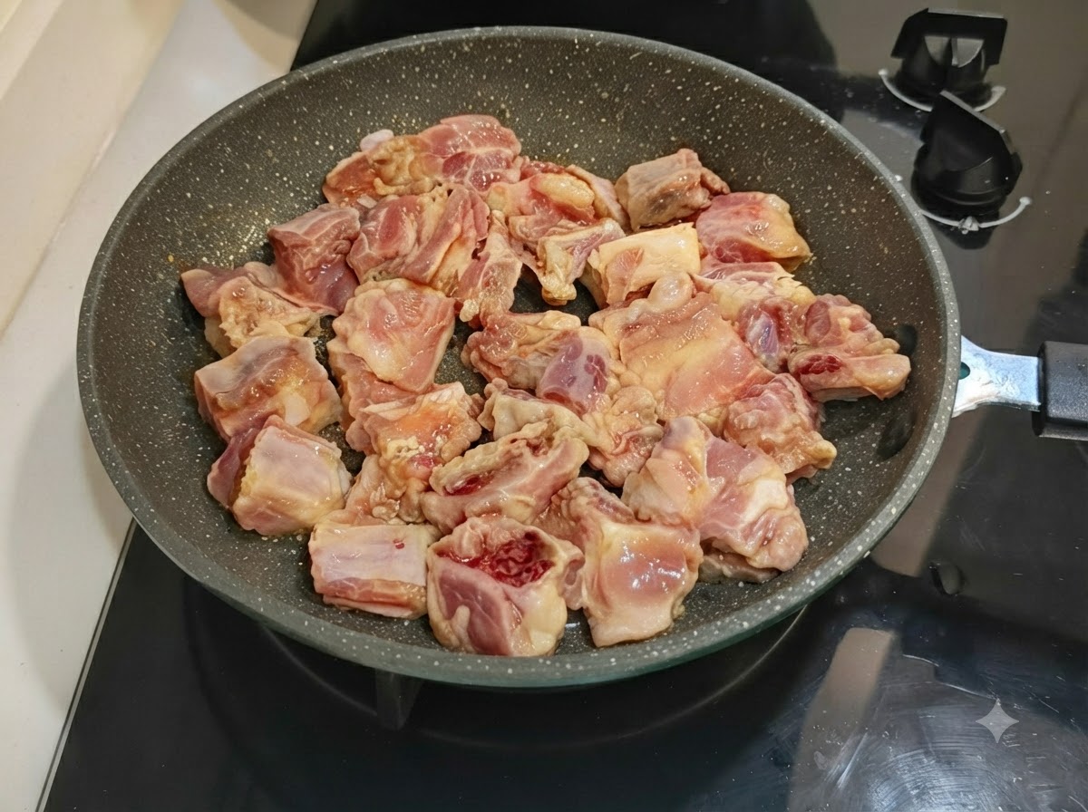 Marinated pork ribs neatly arranged in a speckled frying pan sitting on a stovetop.