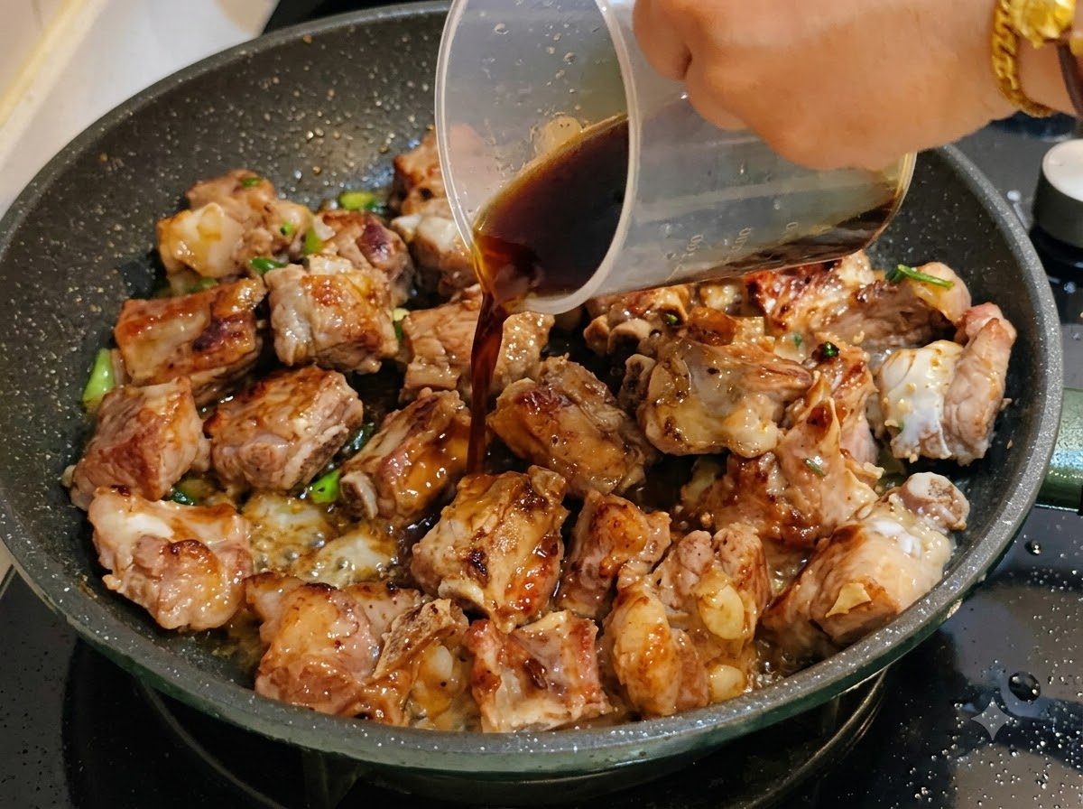 Dark sauce being poured from a measuring cup into the pan with pork ribs.