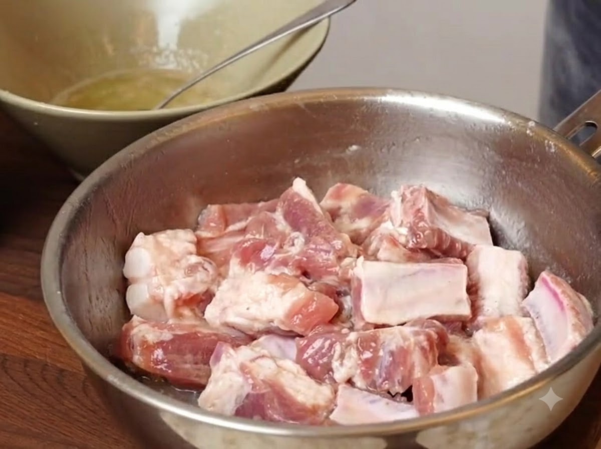Pork rib pieces sitting in a metal bowl with seasoning and starches added before mixing.