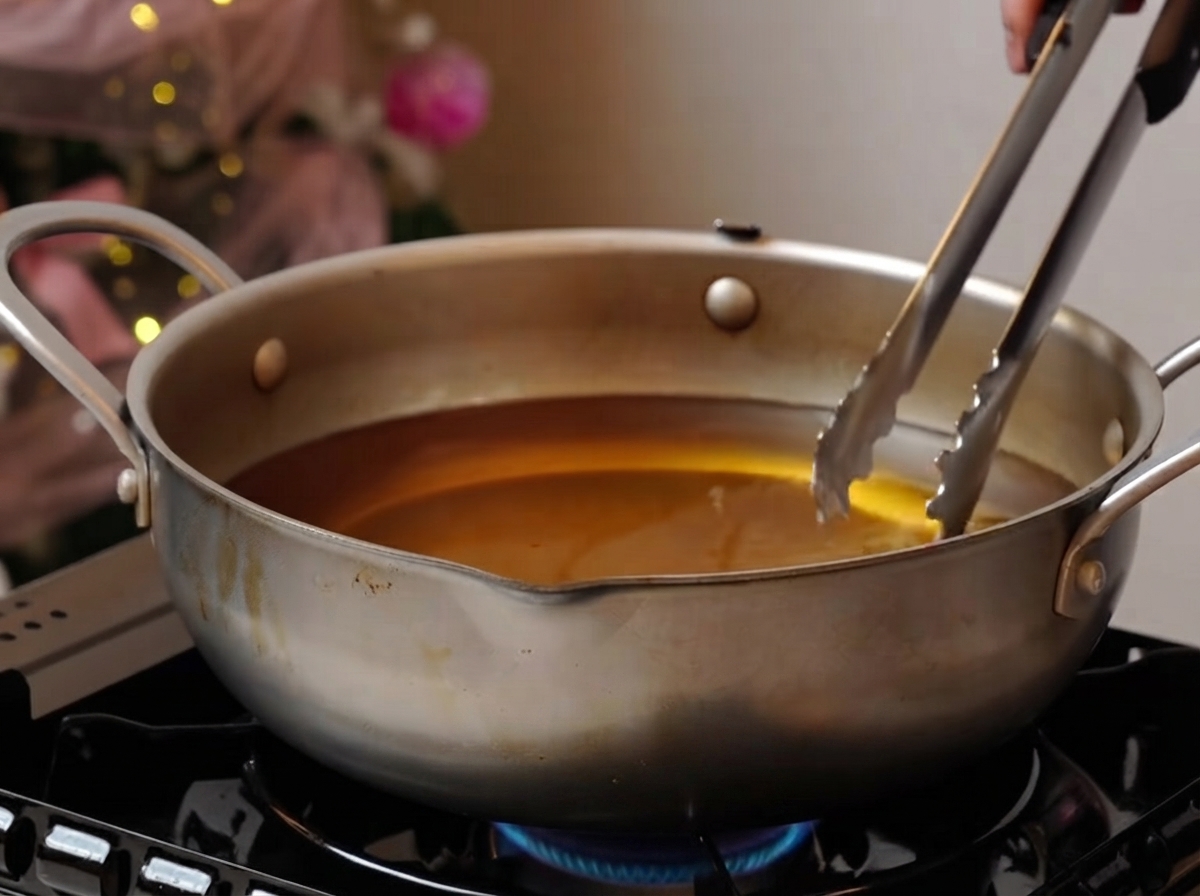 Pork ribs frying gently in a wide pot of oil over a burner.