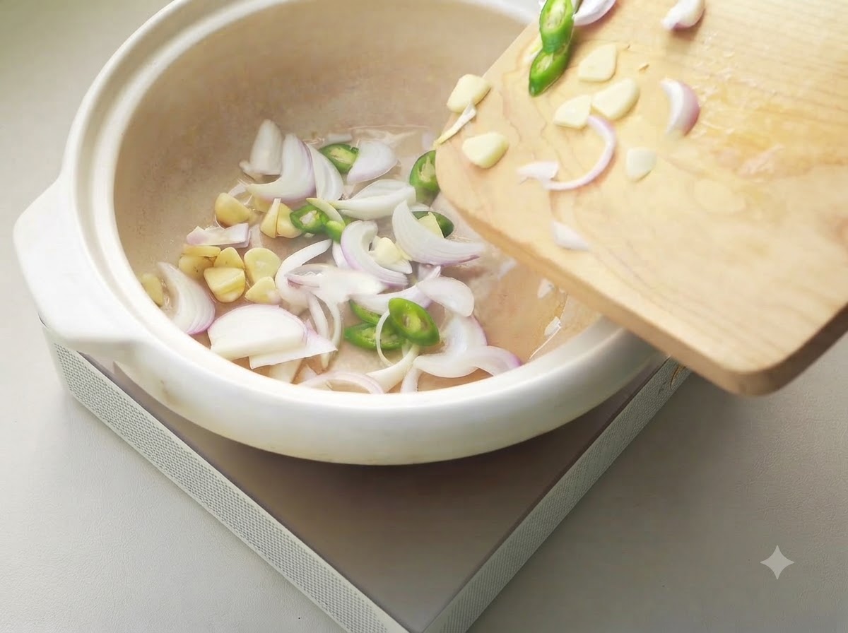 Sliced onions, garlic, and chilies sizzling in a white ceramic pot.