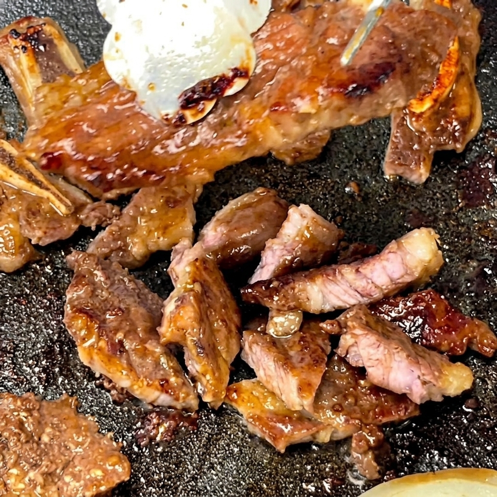 Tongs holding a cooked short rib while scissors slice it into smaller portions on a hot pan.