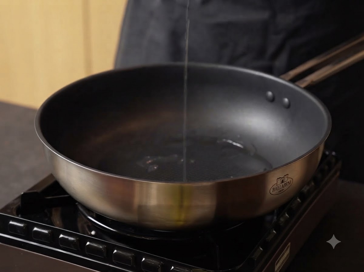 Oil being poured into a hot stainless steel pan on a stove.