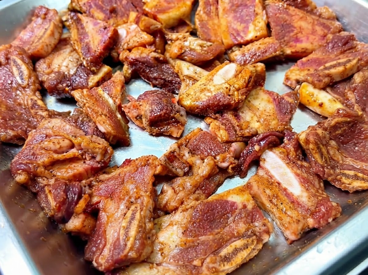 Marinated beef short ribs arranged in a metal tray with shredded onions sprinkled on top.
