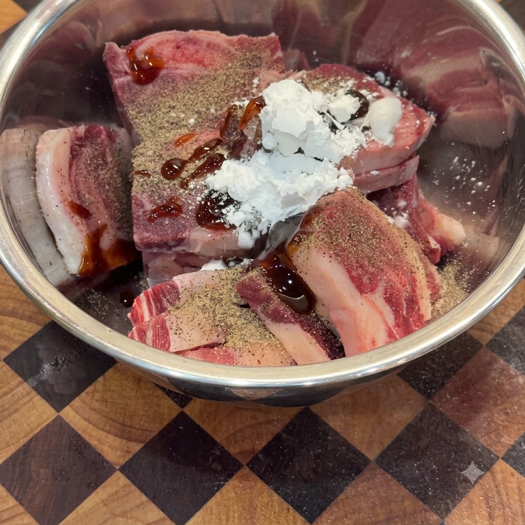 Raw beef pieces in a metal bowl mixed with seasonings, oyster sauce, and cornstarch.