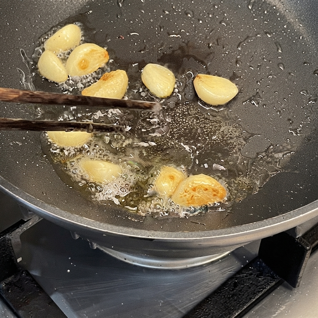 Garlic cloves being sauteed in oil in a hot pan using chopsticks.