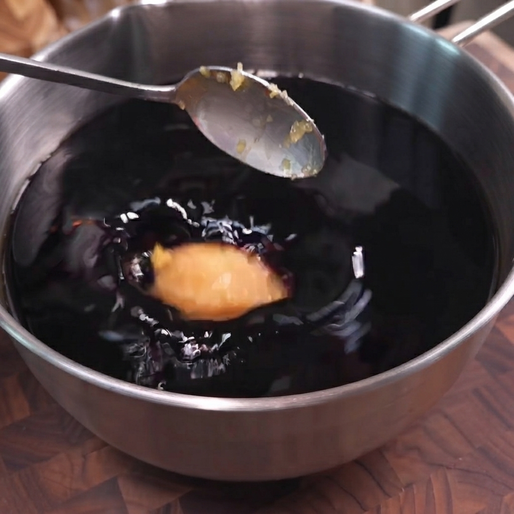 A spoonful of minced garlic being dropped into a pot of dark soy sauce marinade.