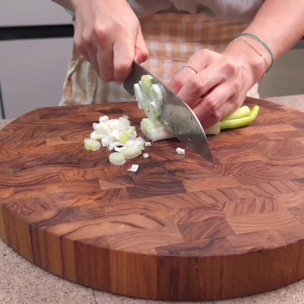 Green onions being chopped on a wooden cutting board with a chefs knife.