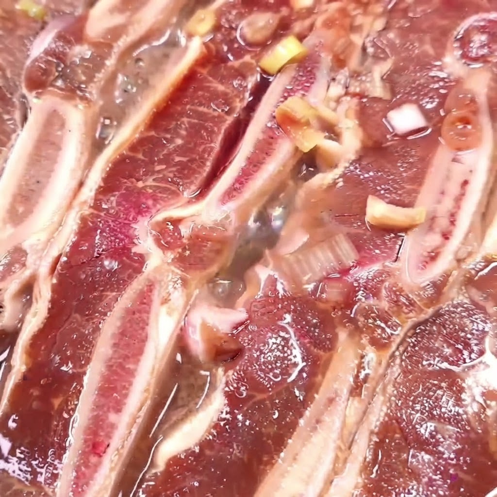 Beef ribs cooking in a pan with bubbling reducing marinade.
