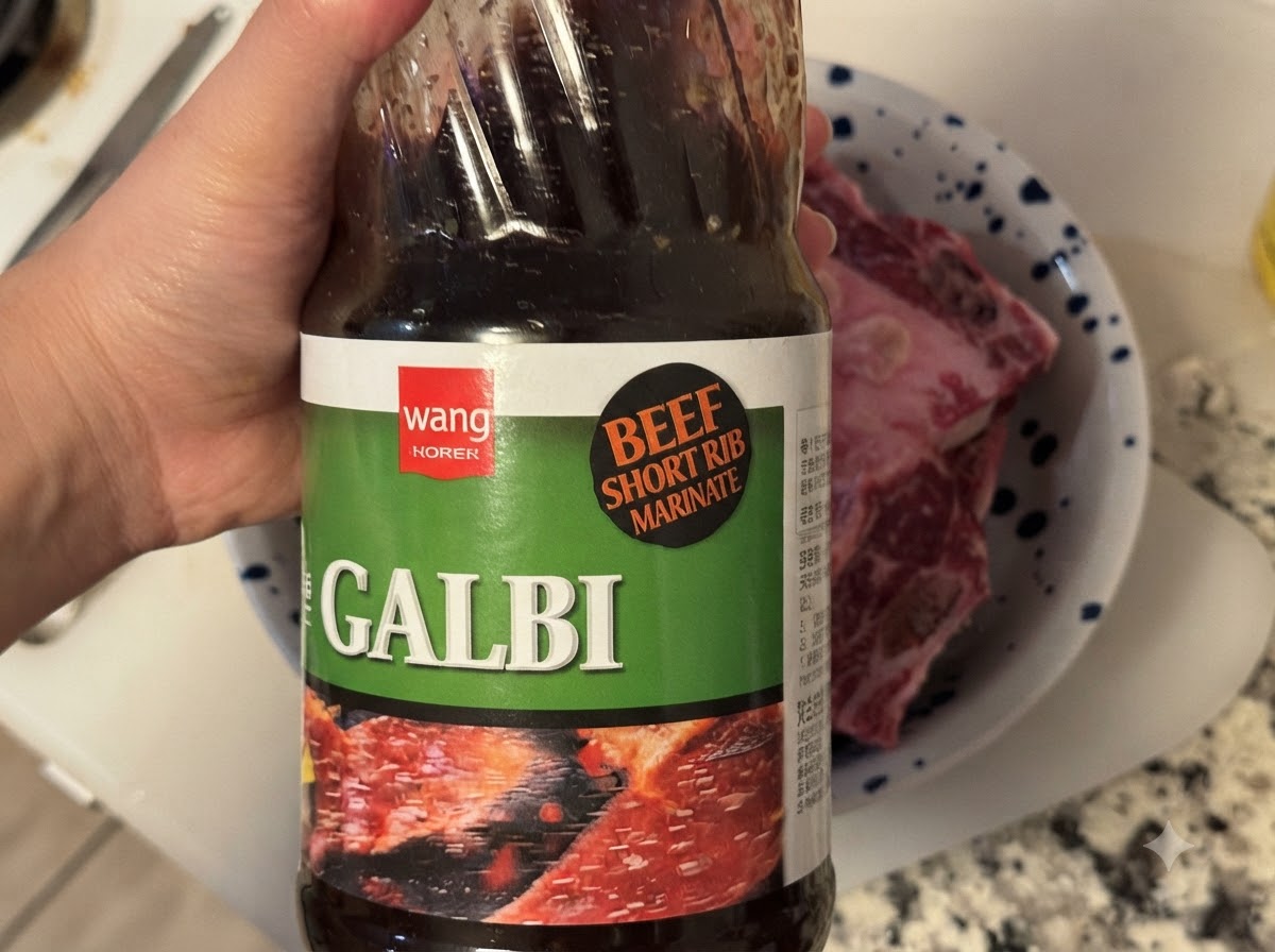 A bottle of Korean BBQ Galbi sauce being poured into a bowl containing raw beef ribs.