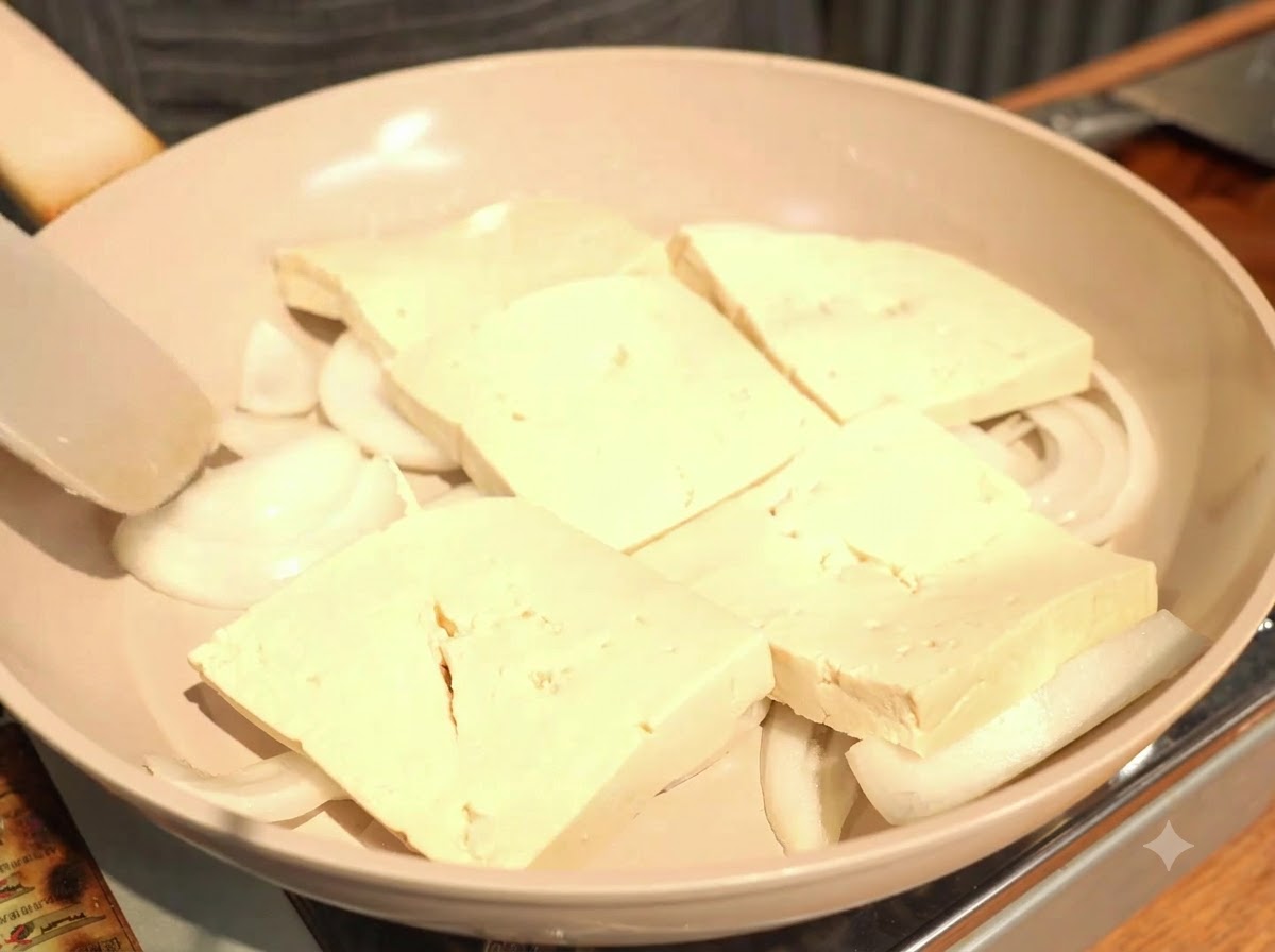 Arranging the thick slices of tofu in a single, slightly overlapping layer on top of the onions.