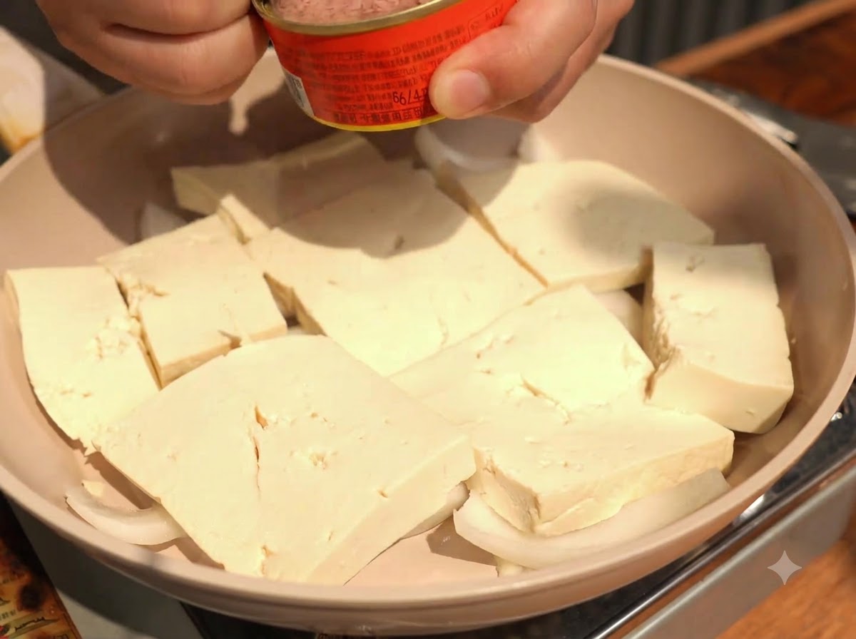 Spooning chunks of canned tuna directly onto the center of the arranged tofu slices.