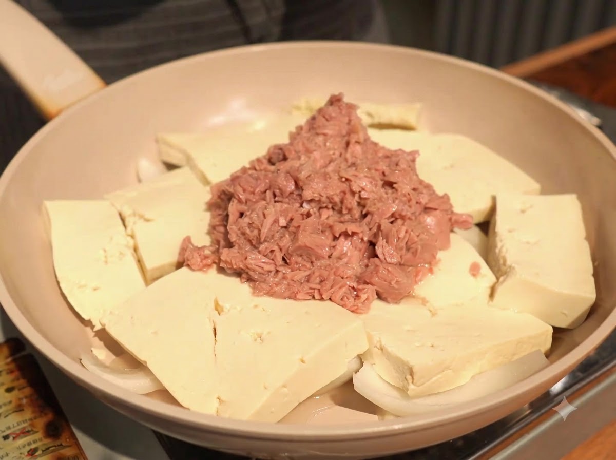 Adding a scoop of minced garlic to the pan, resting it on the tofu alongside the tuna.