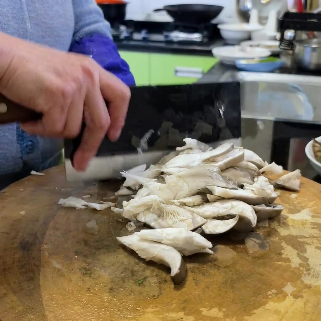 Oyster mushrooms being sliced into smaller portions on a wooden cutting board using a cleaver.