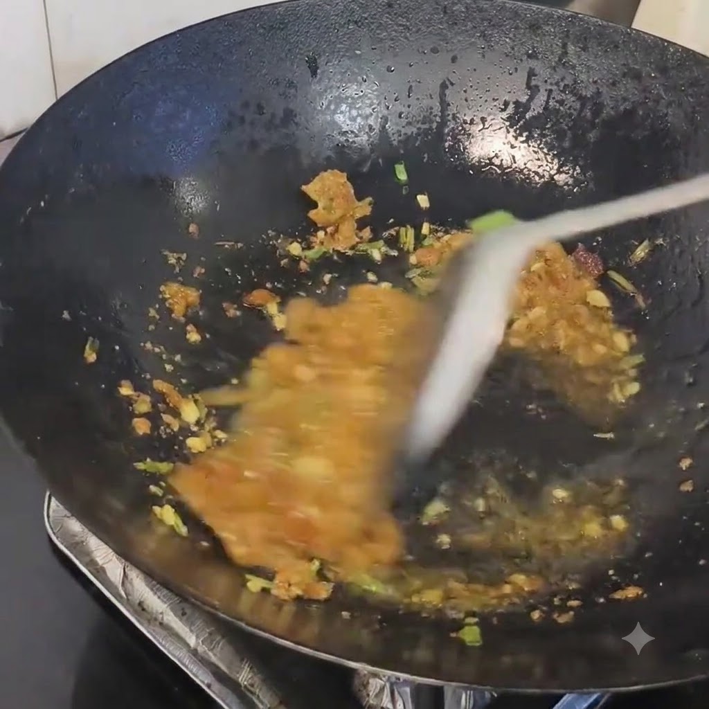 Pork lard residue being mixed into the sautéed aromatics in a hot wok.