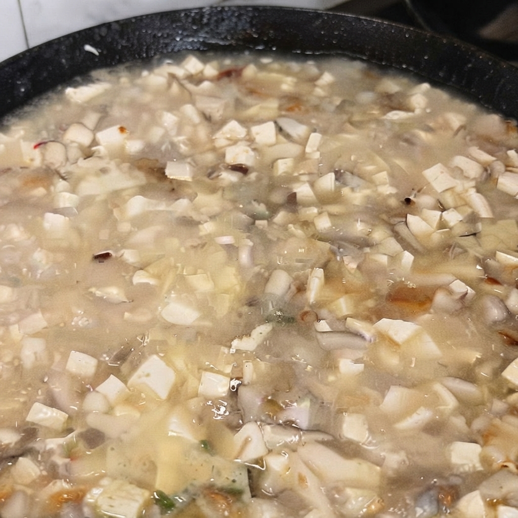 A scoop of MSG being added to the boiling tofu soup.