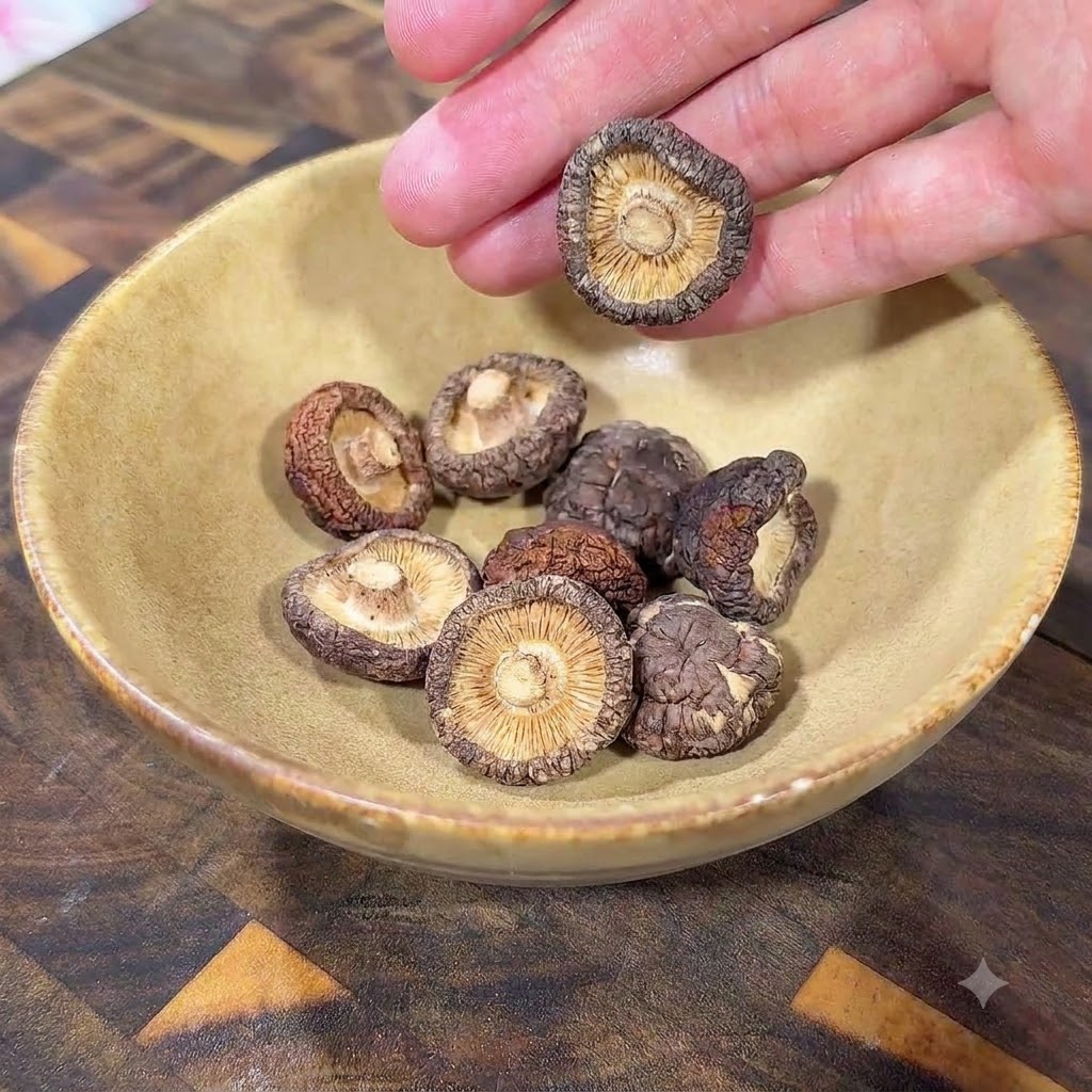 Dry shiitake mushrooms resting inside a yellow ceramic bowl on a wooden surface.