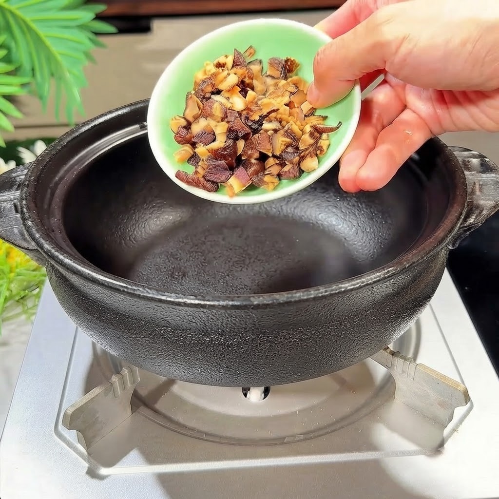 Diced shiitake mushrooms being poured into a heated black clay pot.